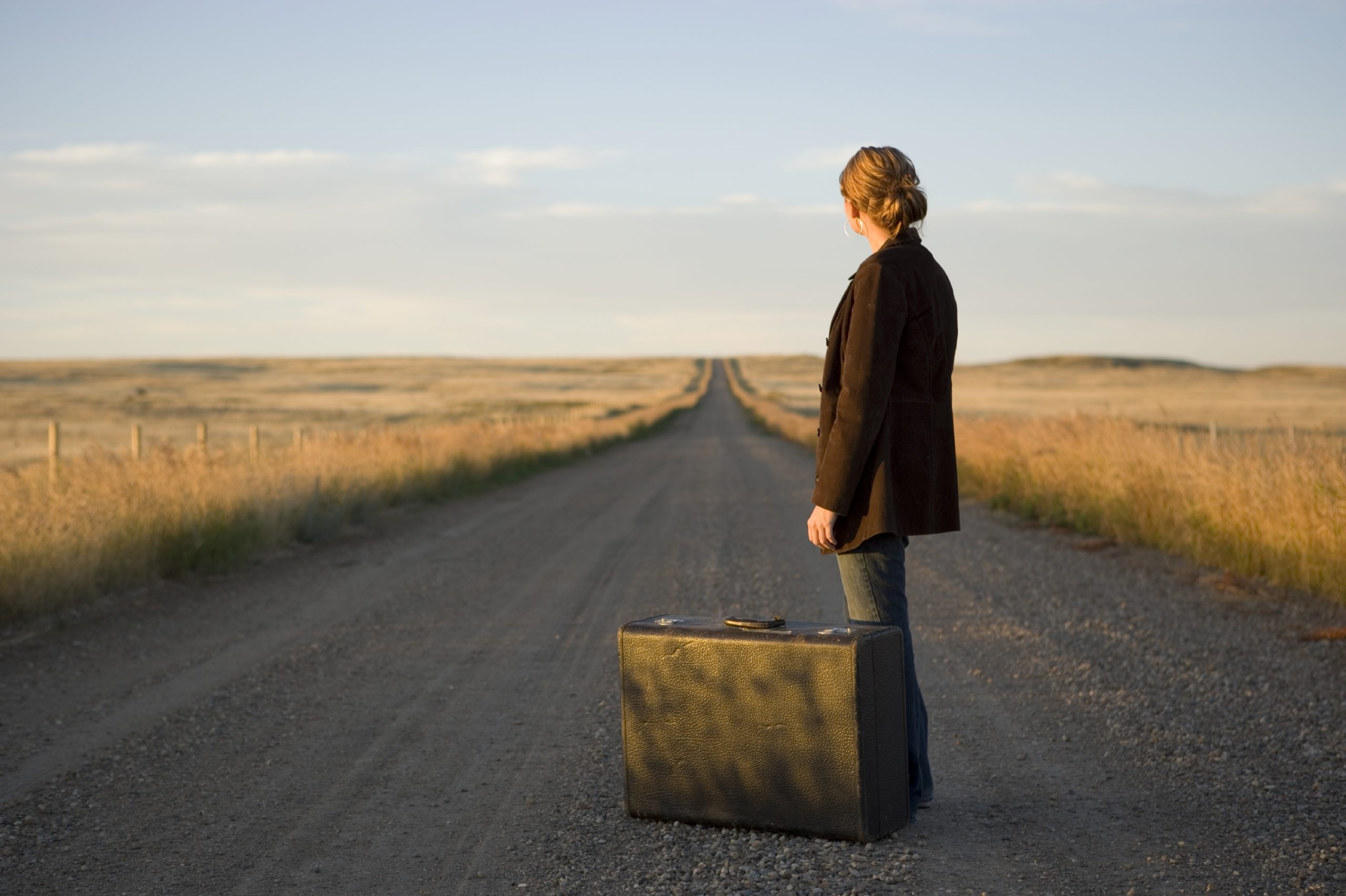 image of woman with a suitcase looking down a long road