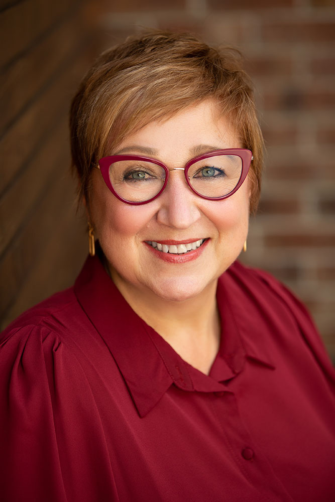 Photo of Mary Yerkes in burgundy shirt and matching glasses smiling<br />
